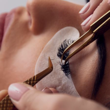 Lash artist creating a volume lash extension set. Isolation tweezers expose the host lash and other tweezers hold volume fan about to be attached. 